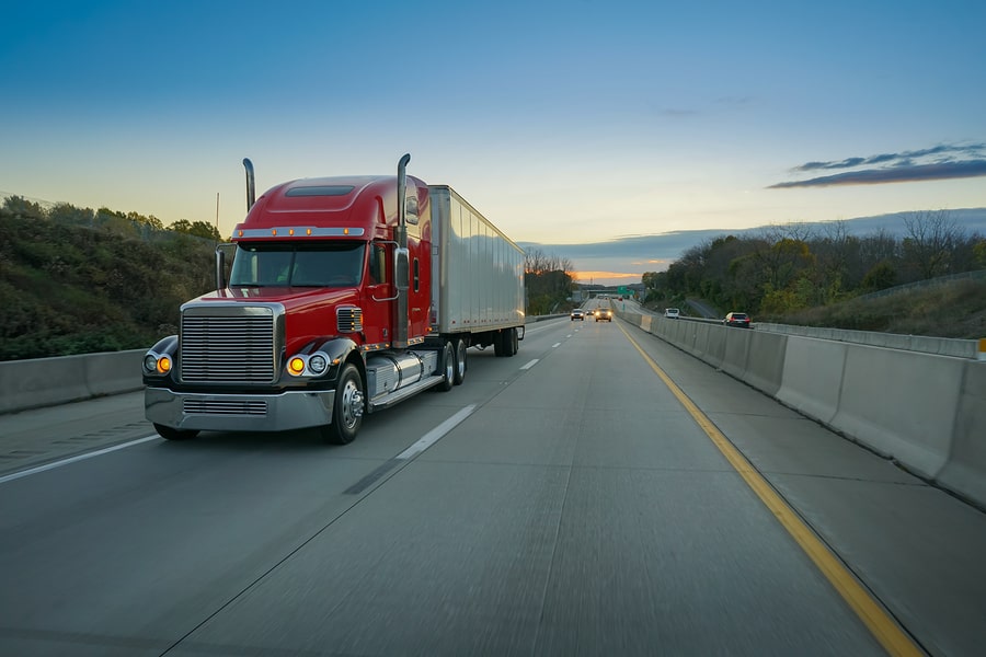 enclosed-auto-transport-carriers A red semi-truck traveling down a highway at sunset.